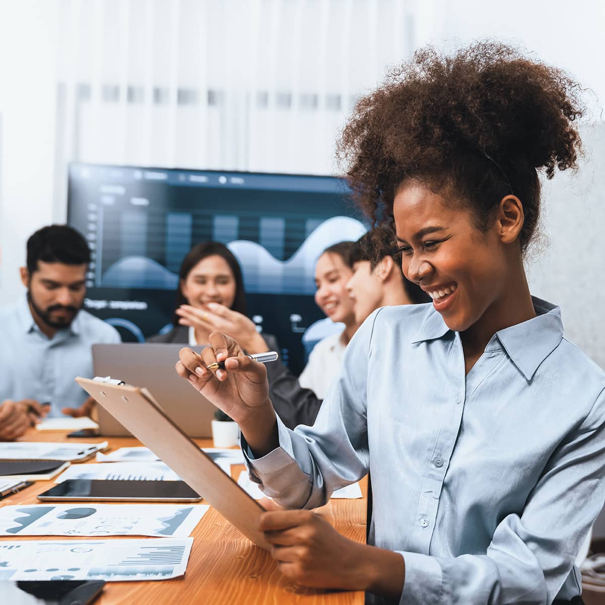 A woman reviews a resume and smiles with her other team members in the background